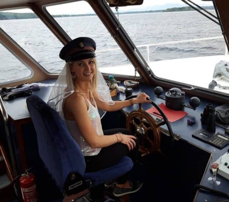 A joyful woman at the helm of a boat on Killarney Lake, wearing a captain's hat and veil.