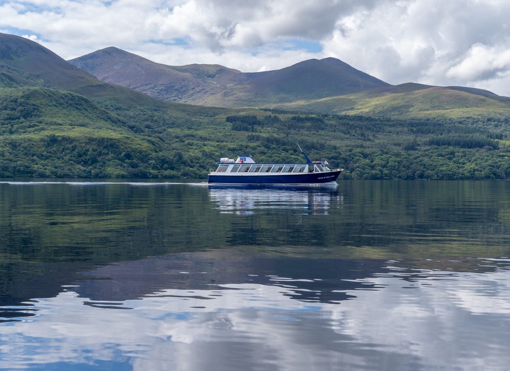 Boat cruising on Killarney Lake beneath rolling hills and a cloudy sky.