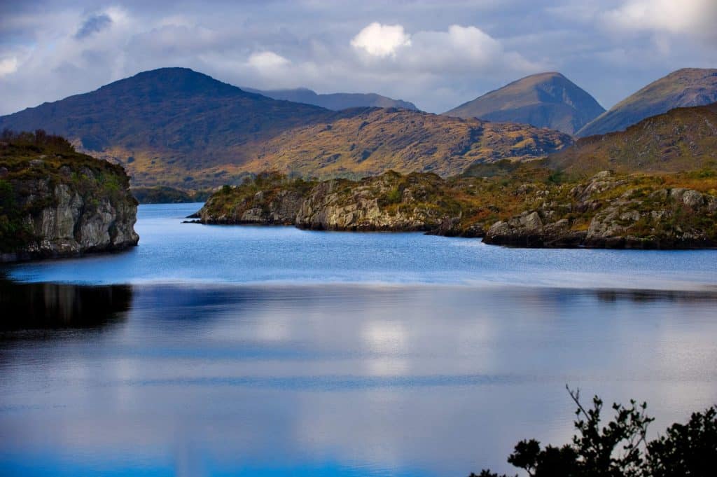 Killarney Lake with serene waters, rugged hills, and cloudy skies, perfect for a scenic tour in Ireland.