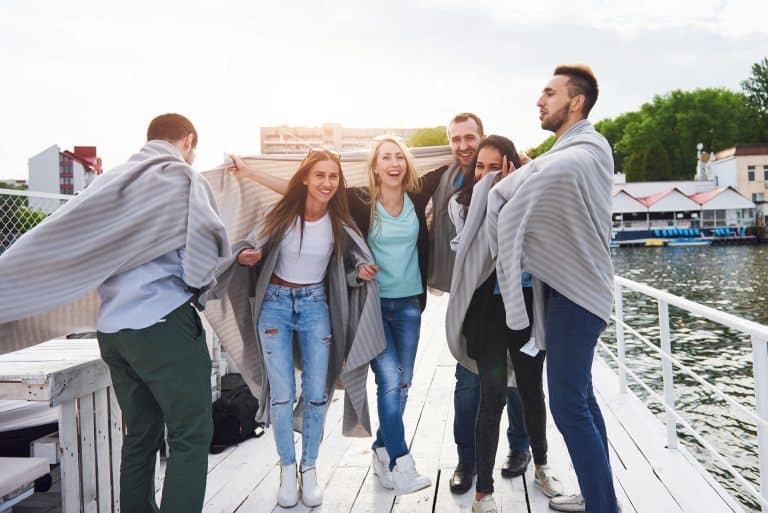 Group enjoying a sunny Killarney Lake Tour, wrapped in blankets on a dock, with water and trees behind them.
